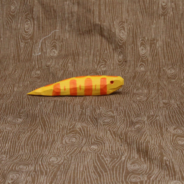 Wooden sculpture of a short and fat yellow snake with orange stripes and a red eye. Its body is akin to a banana slug.