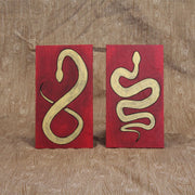 2 red envelopes made out of wood, with painted illustrations on each of gold snakes with black outlines. One snake is curved into itself, akin to the shape of an 8. The other is curved to make a multi-part "S" shape.