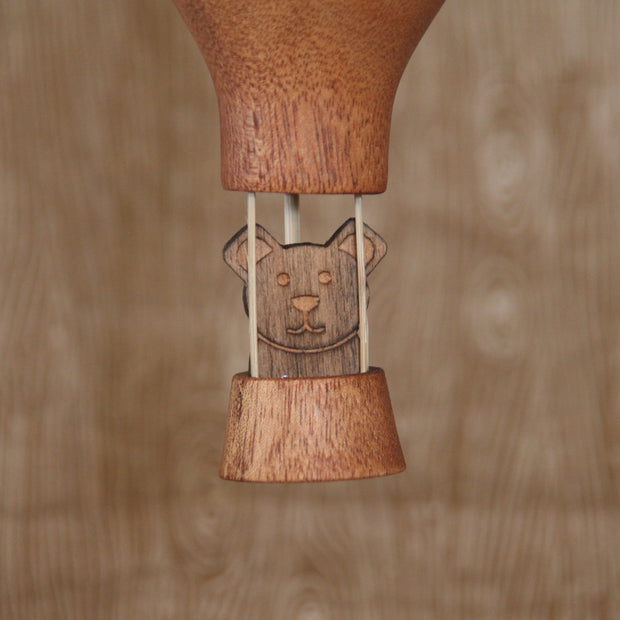 Wooden sculpture of a hot air ballon with a small bear sitting in the basket. 