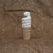 Carved wooden sculpture of a sugar style ice cream cone, holding a curved scoop of white soft serve shaped like a coiled snake. It has rainbow colored sprinkles atop its body.