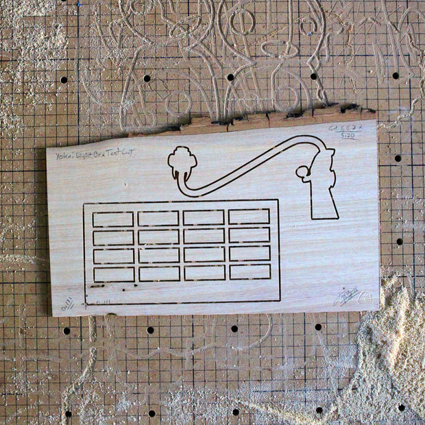 Laser wood cuts on a piece of ash wood of a building with many windows and a strangely shaped character.