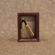 Wooden sculpture of a wooden bat, studded with metal circles and a cloth wrapped handle. It is contained in a shadowbox style wood frame.