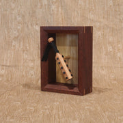 Wooden sculpture of a wooden bat, studded with metal circles and a cloth wrapped handle. It is contained in a shadowbox style wood frame.