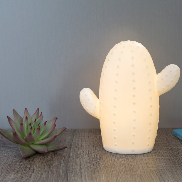 White ceramic lamp in the shape of a cactus with a short and stout body and 2 limbs growing off it. Surface has small dots.