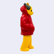 Vinyl figure of with a yellow bear with a humanlike body, standing with his hands in the pockets of a red hoodie. It wears a pair of headphones atop its ears.