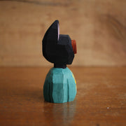 Painted whittled wooden bust of a black cat with red goggles and a teal shirt with a lightning bolt.