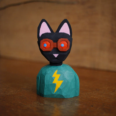 Painted whittled wooden bust of a black cat with red goggles and a teal shirt with a lightning bolt.