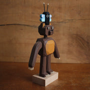 Assembled painted whittled wooden sculpture of a bear with long arms, standing on its hind legs with a small black and blue butterfly atop its head.