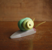 Painted assembled whittled wood sculpture of a gray snail with a green swirled shell and 2 large feelers atop its head.