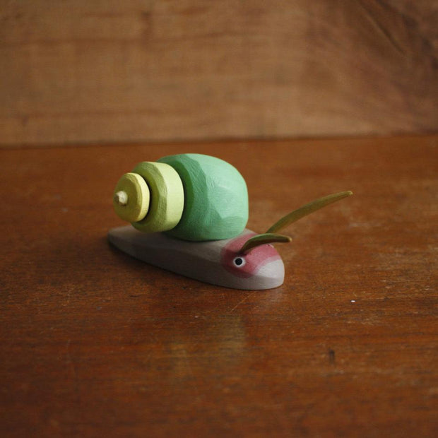 Painted assembled whittled wood sculpture of a gray snail with a green swirled shell and 2 large feelers atop its head.