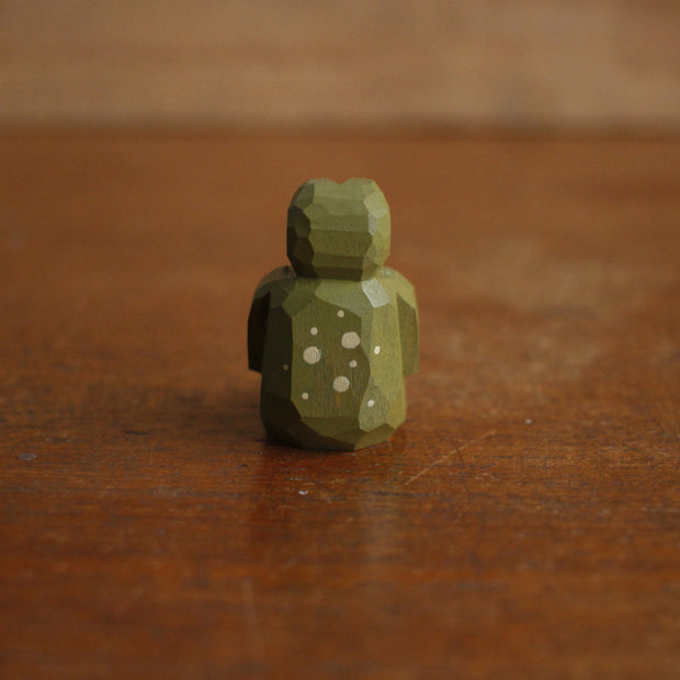 Small painted whittled wood sculpture of a green frog, sitting on the ground with its legs extended out in front and its hands over its stomach.