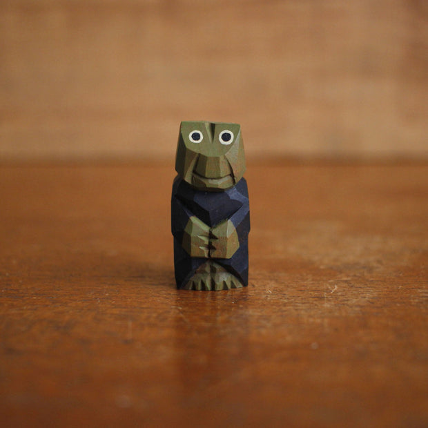 Very small painted whittled wooden sculpture of a frog wearing a navy blue robe and with a content expression and its hands folded.