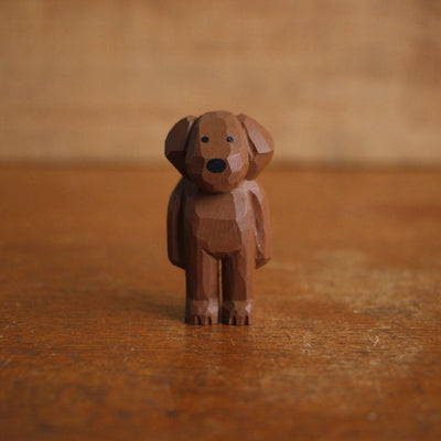 Small painted whittled wooden sculpture of a cute brown dog with floppy ears, standing like a person. It has a set of very small black eyes and a large black nose.