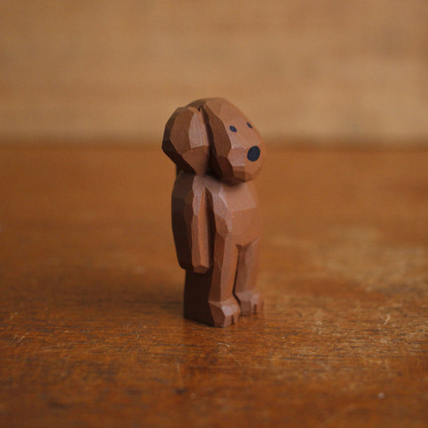 Small painted whittled wooden sculpture of a cute brown dog with floppy ears, standing like a person. It has a set of very small black eyes and a large black nose.