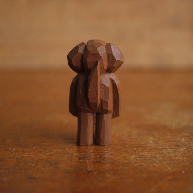 Small painted whittled wooden sculpture of a cute brown dog with floppy ears, standing like a person. It has a set of very small black eyes and a large black nose.