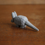 Small whittled wooden sculpture, painted gray, of an armadillo with a rigid back and long tail. It has a simple pair of small black eyes and tall pointed ears.