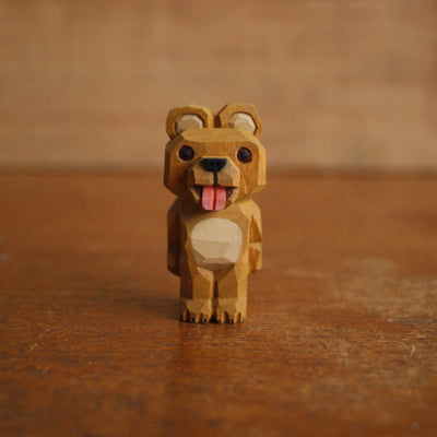 Painted whittled wooden sculpture of a cute brown bear with a large head, standing on its hind legs like a human. It has its tongue out.