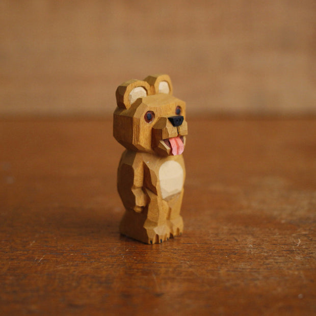 Painted whittled wooden sculpture of a cute brown bear with a large head, standing on its hind legs like a human. It has its tongue out.