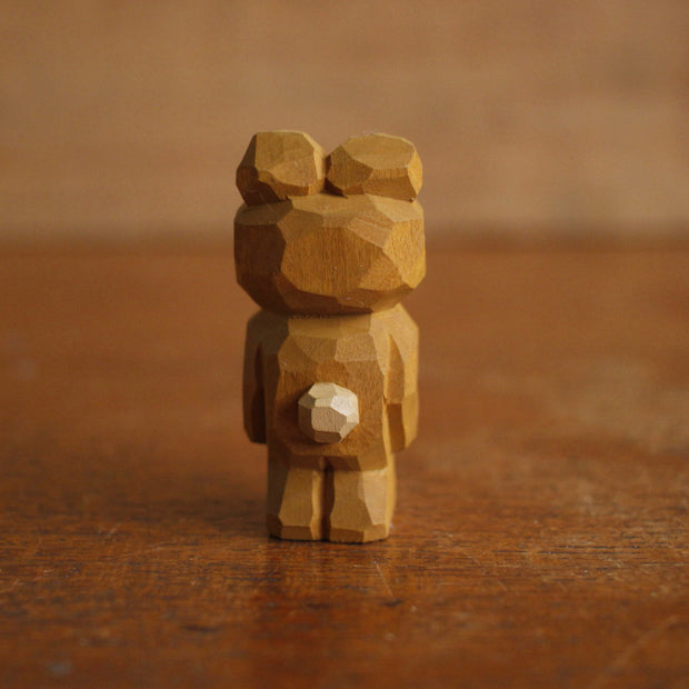 Painted whittled wooden sculpture of a cute brown bear with a large head, standing on its hind legs like a human. It has its tongue out.