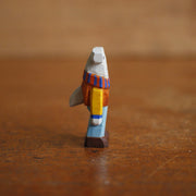 Small painted whittled wooden sculpture of a hammerhead shark, standing on 2 legs like a human and wearing a striped scarf, orange sweater, and blue jeans. It smiles and looks off to the side.