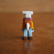 Small painted whittled wooden sculpture of a hammerhead shark, standing on 2 legs like a human and wearing a striped scarf, orange sweater, and blue jeans. It smiles and looks off to the side.