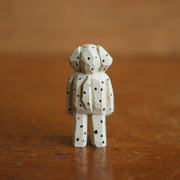 Tiny painted whittled wooden sculpture of a dog with floppy ears, standing on its hind legs like a human. Its white with many black spots, and a small pair of black eyes and a large nose.