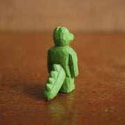 Small painted whittled wooden sculpture of a green gator, standing on 2 legs like a human with a strong body. It has a blank expression and its arms hang at its sides.