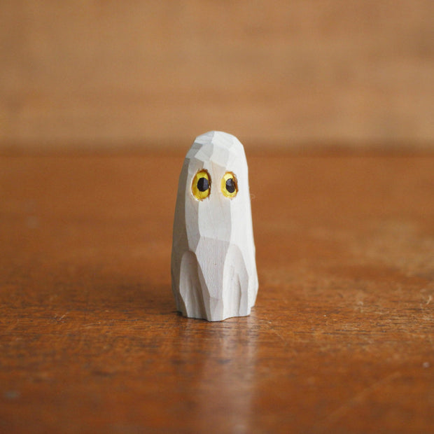 Small whittled wooden sculpture of a ghost, covered in a white sheet, with a pair of yellow eyes looking off to the side.