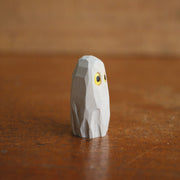 Small whittled wooden sculpture of a ghost, covered in a white sheet, with a pair of yellow eyes looking off to the side.