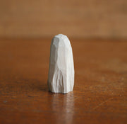 Small whittled wooden sculpture of a ghost, covered in a white sheet, with a pair of yellow eyes looking off to the side.