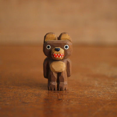 Small whittled wooden sculpture of a brown bear, standing on its hind legs like a human with its arms at its side. It has a wide red mouthed smile with small teeth.