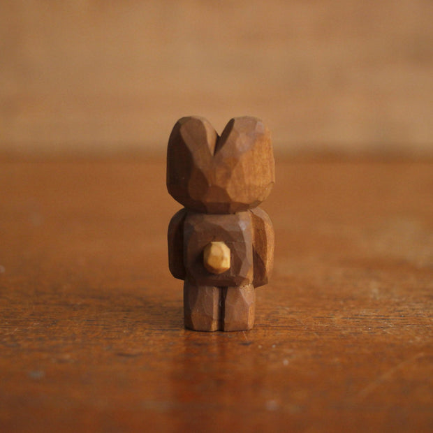 Small whittled wooden sculpture of a brown bear, standing on its hind legs like a human with its arms at its side. It has a wide red mouthed smile with small teeth.