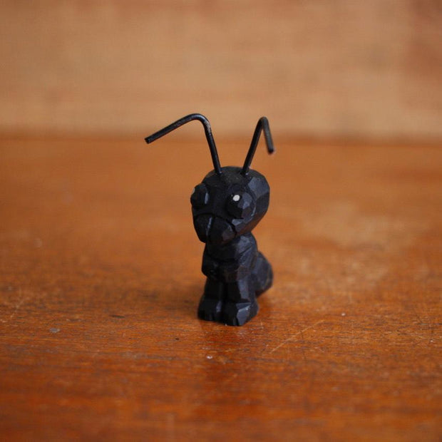 Small painted whittled wooden sculpture of a black ant with bent wires for antenna. 