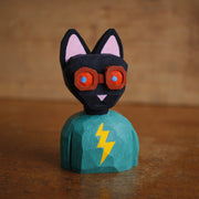 Painted whittled wooden bust of a black cat with red goggles and a teal shirt with a lightning bolt.