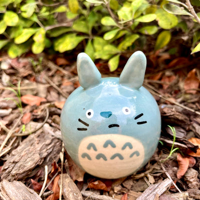 Ceramic sculpture of Totoro with a rounded body and a painted on cute face. His ears jut out from his head.