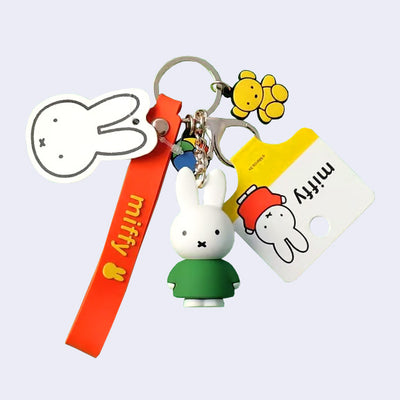 Keychain with many rubber charms attached to it in addition to a lobster clasp and keychain: Miffy figure in a green dress, Miffy strap, flat mini ball and flat mini teddy bear