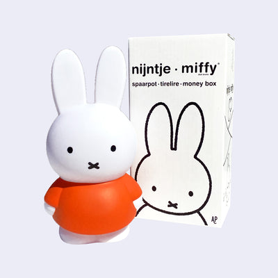 Coin bank shaped like Miffy, wearing her standard orange dress. She stands next to the product packaging.