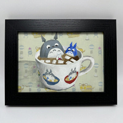 Painting of a white mug with hot chocolate within it and marshmallows. 3 Totoro characters sit within it - gray, blue and white descending in size. 