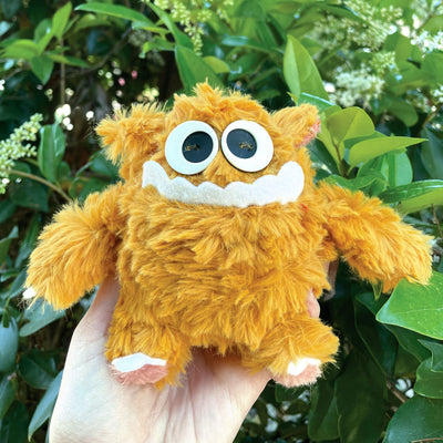 Fluffy plush doll of a yellow monster with lots of fur and a pair of big cartoon eyes and a goofy underbite smile.