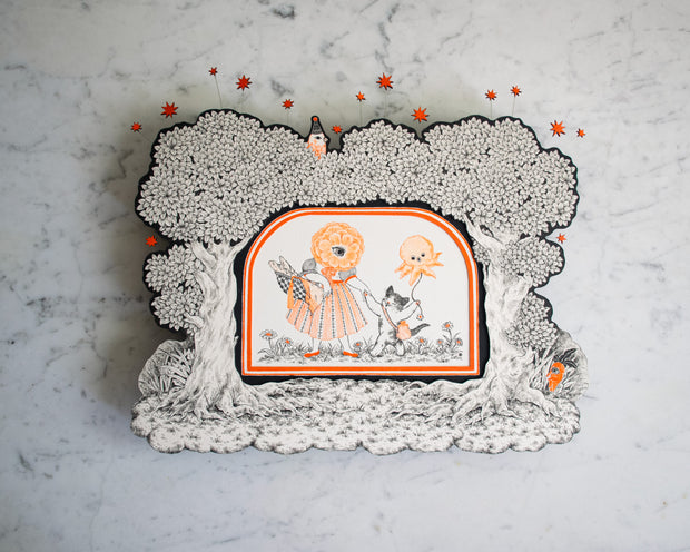 Black and orange ink illustration of a flower person wearing a dress and holding hands with a cute cat, which holds an octopus shaped balloon. The pair are framed by cut out trees and attached stars.