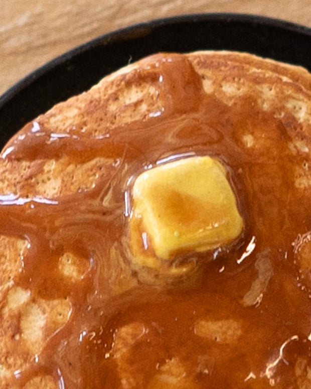 Small assembled clay sculpture of a model pancake breakfast on a plate. A pat of butter rest atop the stack with syrup poured over the pancakes. Detail shot.