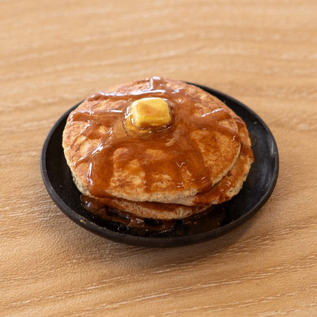 Small assembled clay sculpture of a model pancake breakfast on a plate. A pat of butter rest atop the stack with syrup poured over the pancakes.