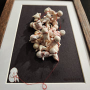 Framed sculpture of many faceless simplistic humanoid characters, all tied up with one another by a red string. The red string falls to the bottom, where a painting of a small character covering their face sits.