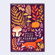 Spiral bound calendar cover, plum purple with autumn colored illustrations of botanicals, mushrooms and a fox, mouse and snail.