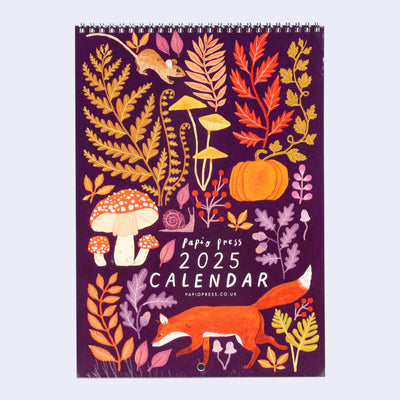 Spiral bound calendar cover, plum purple with autumn colored illustrations of botanicals, mushrooms and a fox, mouse and snail.