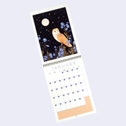 Spiral bound calendar for the month of January, with one page being a full bleed illustration and the other having space for writing in each day. Illustration features a night scene of a barn own sitting on a stump in front of blue flowers under a full moon.