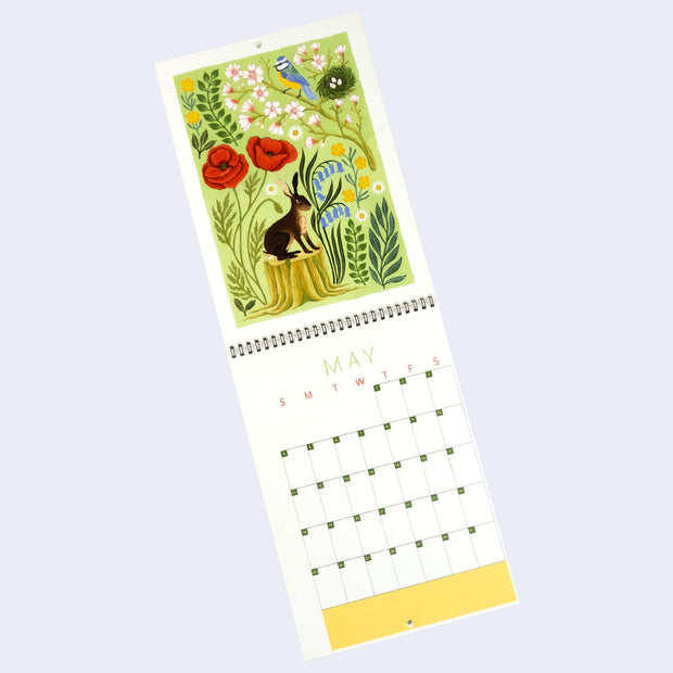 Spiral bound calendar for the month of May, with one page being a full bleed illustration and the other having space for writing in each day. Illustration is pastel green with a rabbit sitting on a log and several botanicals all around, laid flat like a collage of sorts.