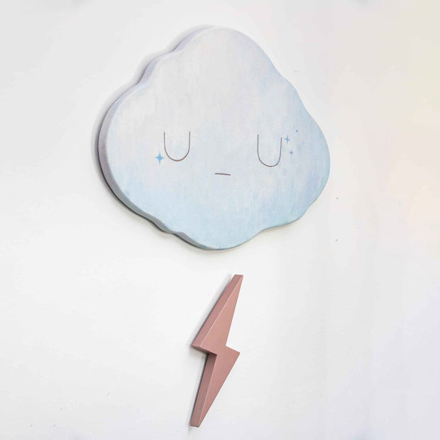 2 die cut wooden panels, one shapes like a cloud and painted light blue with a simple closed eye expression. Below, is a champagne pink colored lightning bolt.