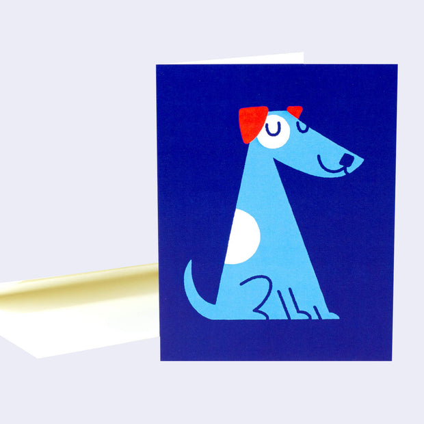 Greeting card, bright blue with a simplistic illustration of a blue dog with white spots and red ears, sitting and smiling with its eyes closed.