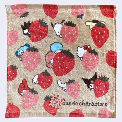 Tan towel with a repeating pattern of large red and pink strawberries. Behind the strawberries are Sanrio characters, peeking out.